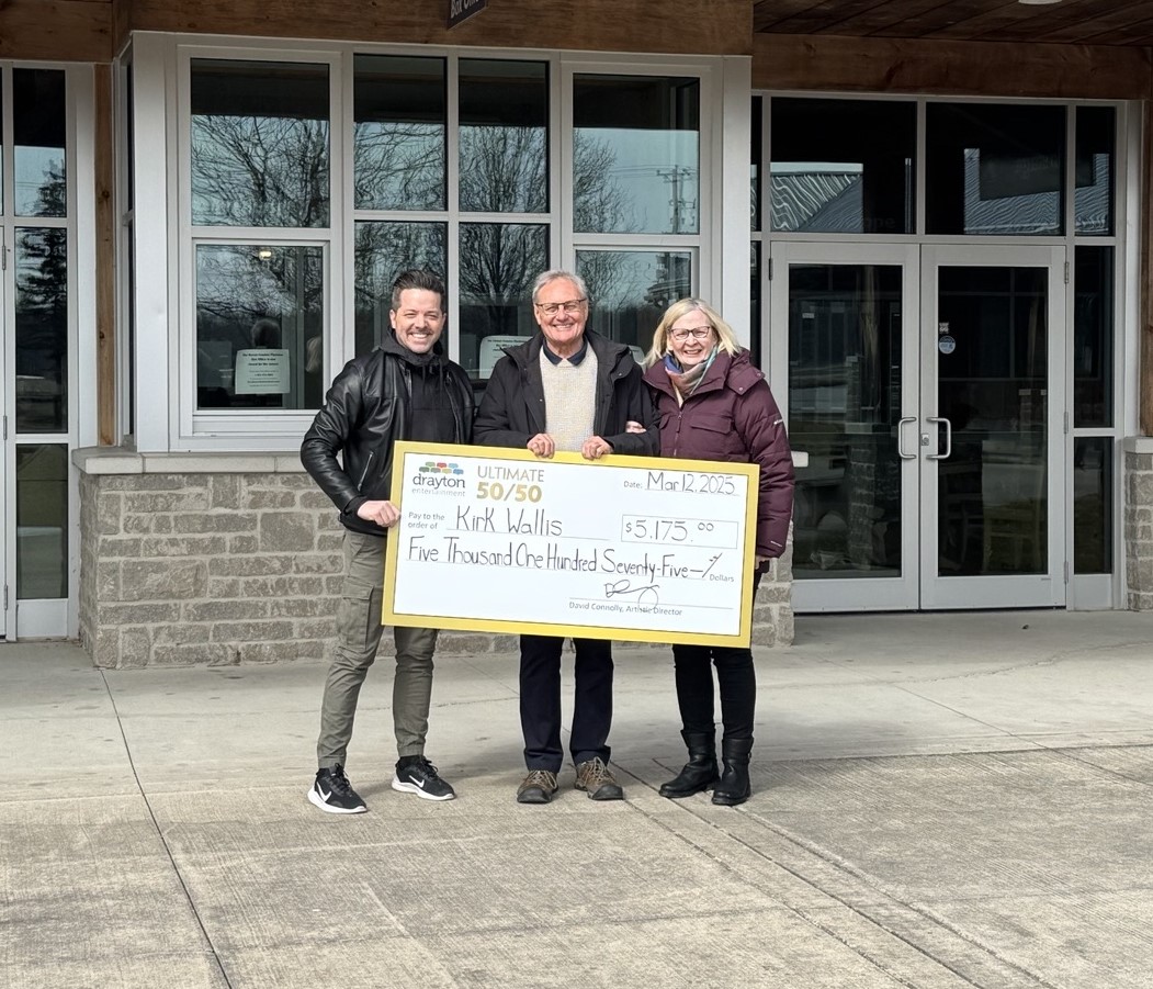 Three people pose outdoors in front of a building, holding an oversized check. The check, made out to Kirk Wallis, is for $5,175.00 from the "drayton ULTIMATE 50/50" lottery, dated March 12, 2025.